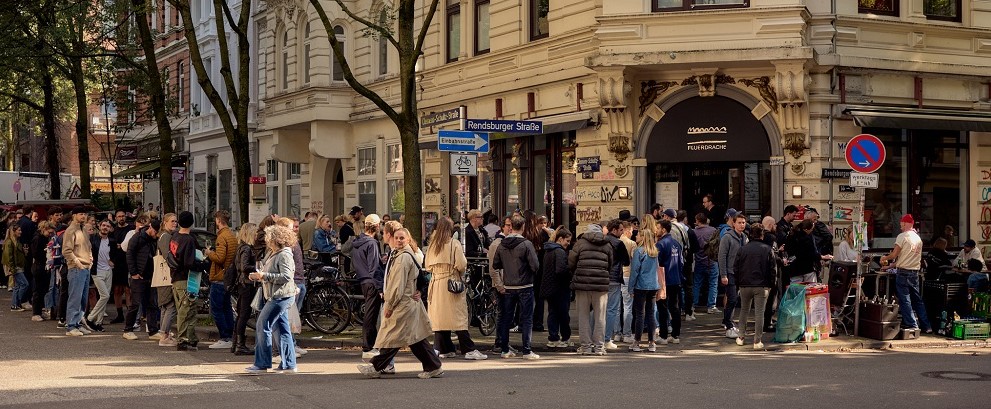 Lange Schlange vor einem beliebten Food-Hotspot im Hamburger Schanzenviertel bei sonnigem Wetter.