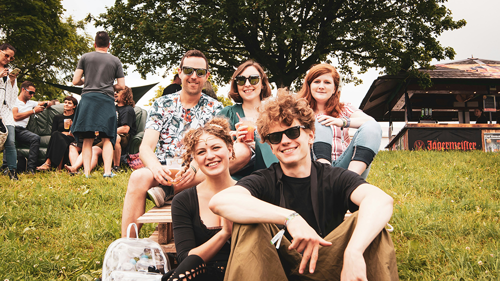 Group of young people sitting and laughing on a grassy lawn outdoors.